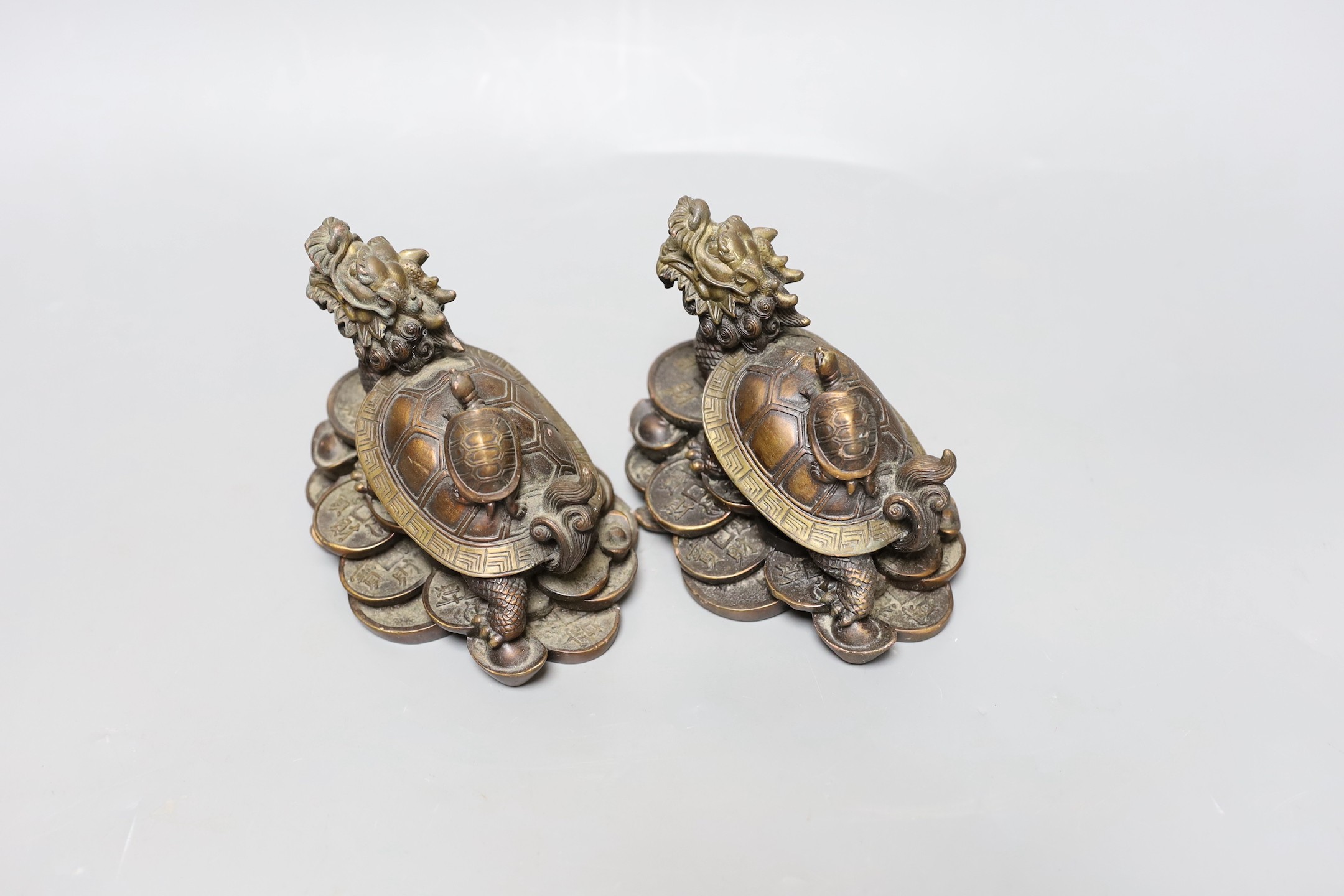 Two Chinese bronze models of dragon turtles on a pile of cash, 10cm